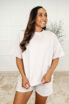 A woman wearing a sand beige ribbed knit set with a banded round neckline and exaggerated banded cuffs, including functional side pockets.