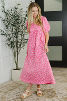Woman wearing a pink floral dress standing indoors with a plant in the background