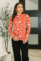 Woman wearing a vermillion long sleeve top with a floral pattern and lettuce hem.
