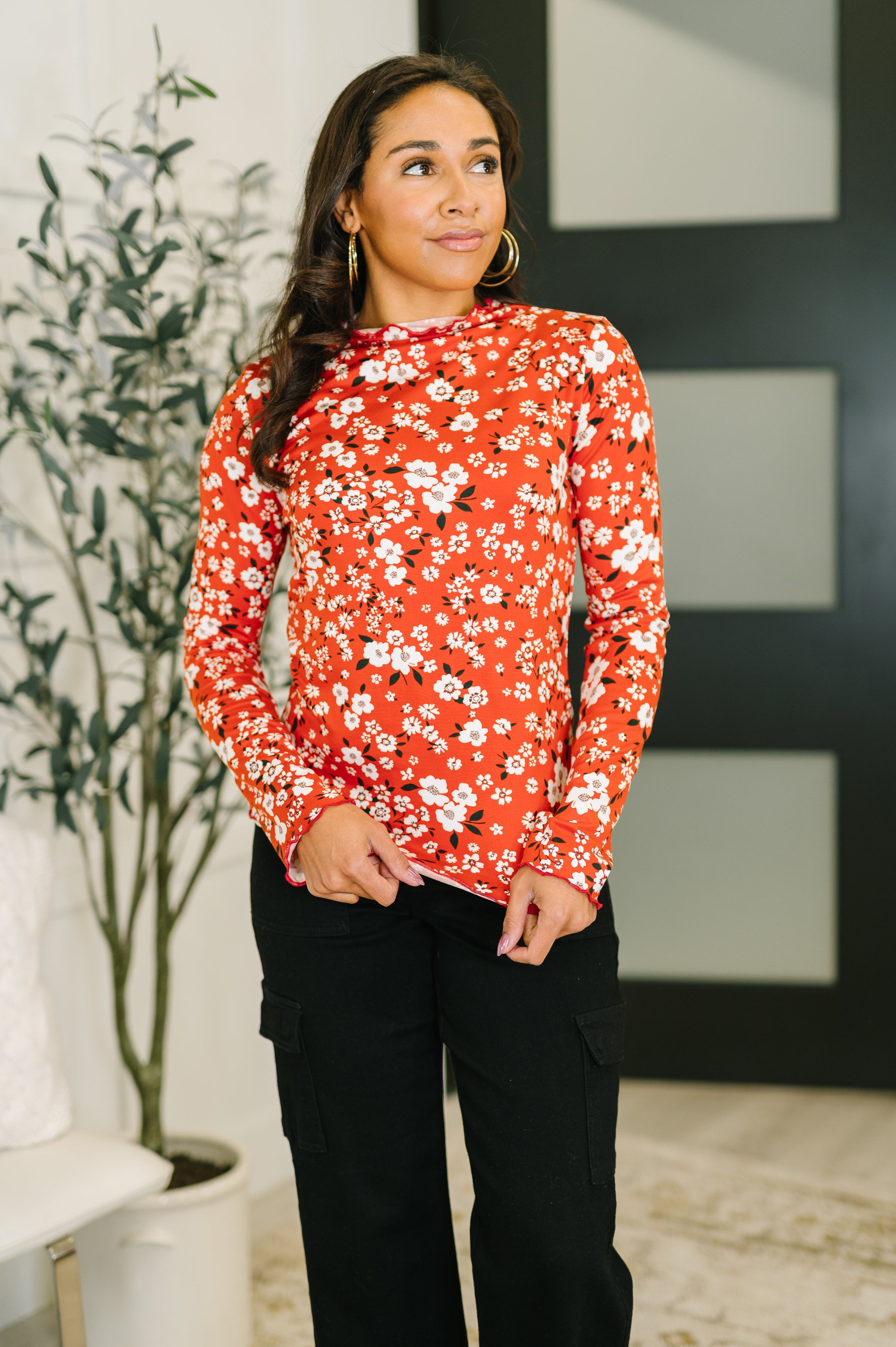 Woman wearing a vermillion long sleeve top with a floral pattern and lettuce hem.