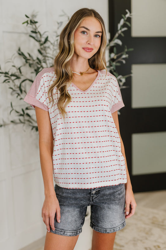 Woman wearing a striped shirt and denim shorts standing indoors with decorative elements in the background