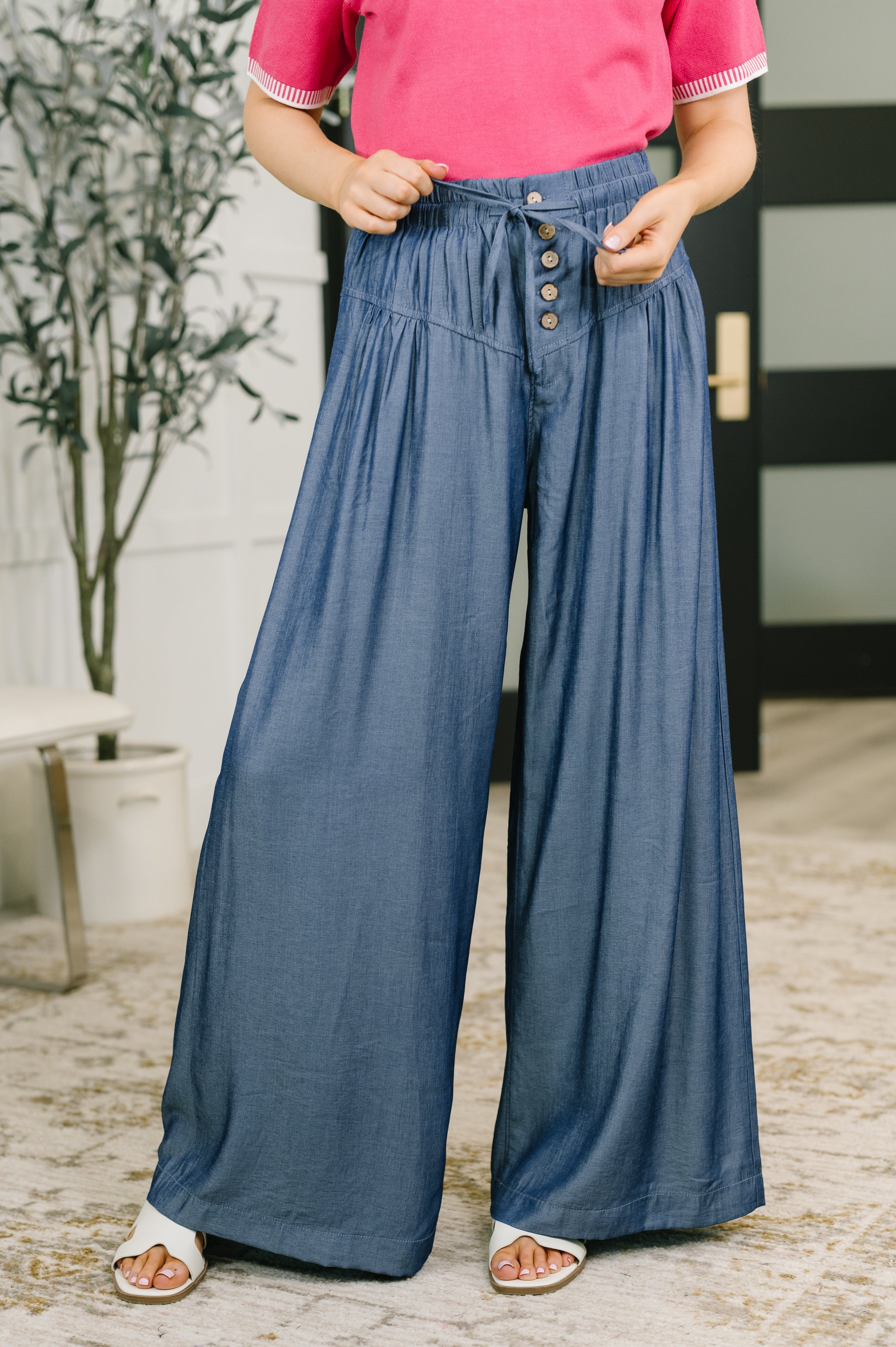 Wide-leg blue bottoms with a high-waisted fit, button closures, and pleat details.
