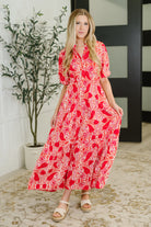 Woman wearing a red patterned dress standing indoors with a plant in the background
