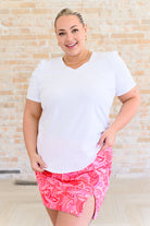 A woman wearing a white v-neck tee shirt and a pink floral mini skirt.
