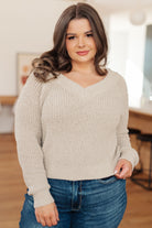 Neutral V-neck sweater with a soft knit and loose fit, worn by a model with jeans in a casual indoor setting.
