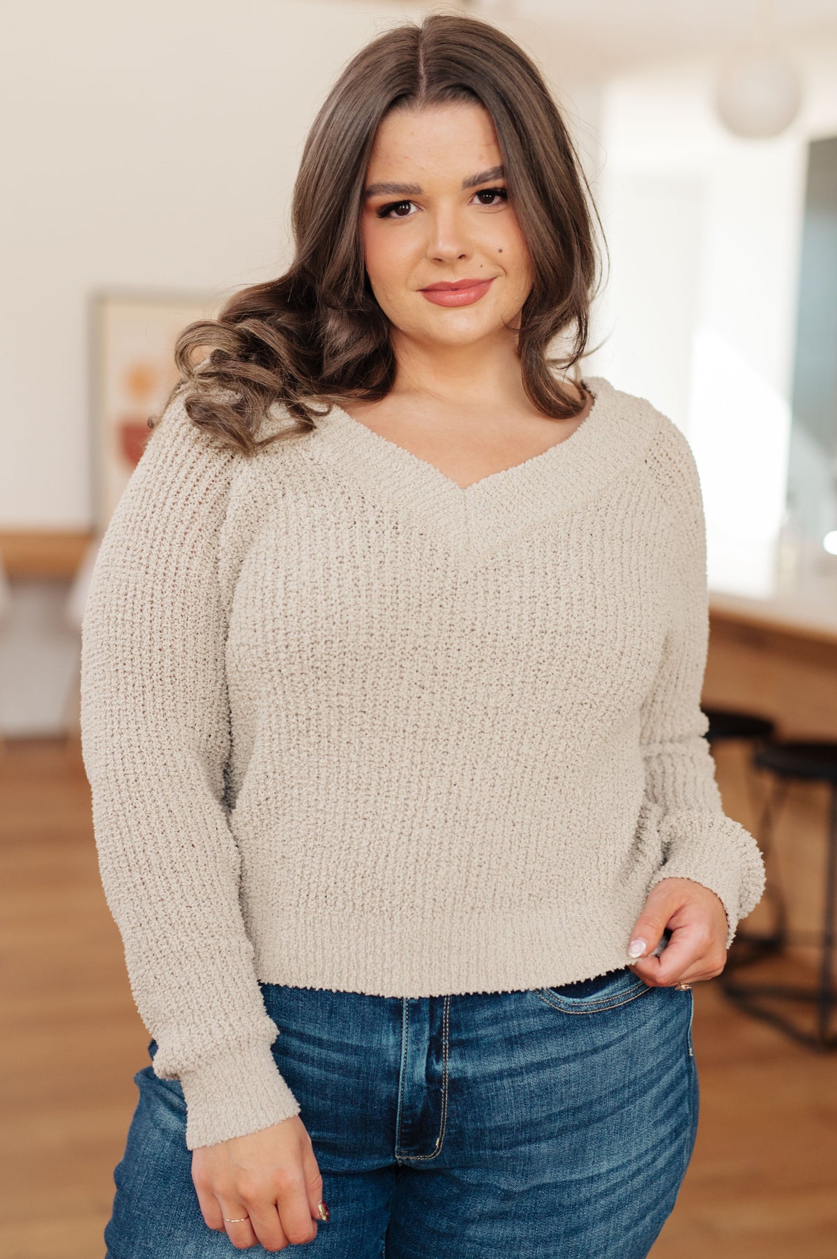 Neutral V-neck sweater with a soft knit and loose fit, worn by a model with jeans in a casual indoor setting.