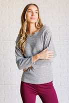 Woman wearing a gray long sleeve top with boat neckline and dolman sleeves.