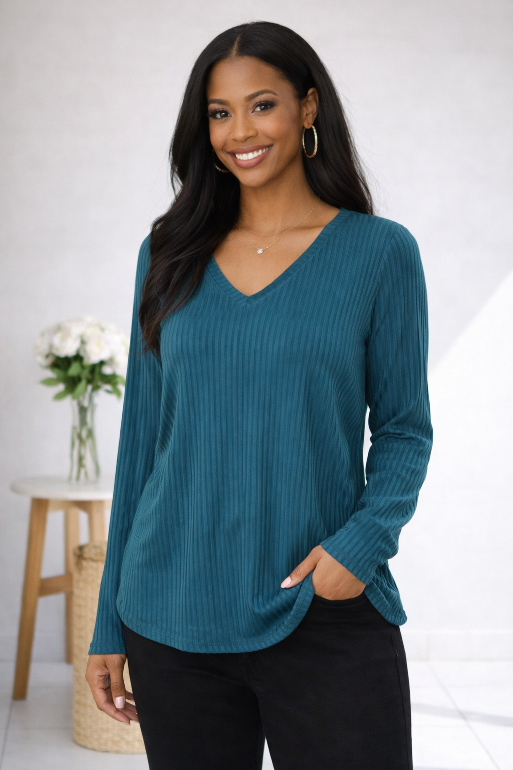 A woman wearing a teal green, subtly striped long sleeve top with a v-neckline and relaxed fit.