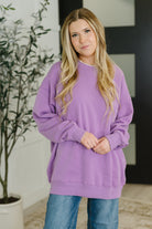 Woman wearing a purple sweater standing indoors with a plant in the background