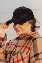 Black sherpa ball cap with a boucle texture and adjustable velcro back on a person wearing a plaid shirt.