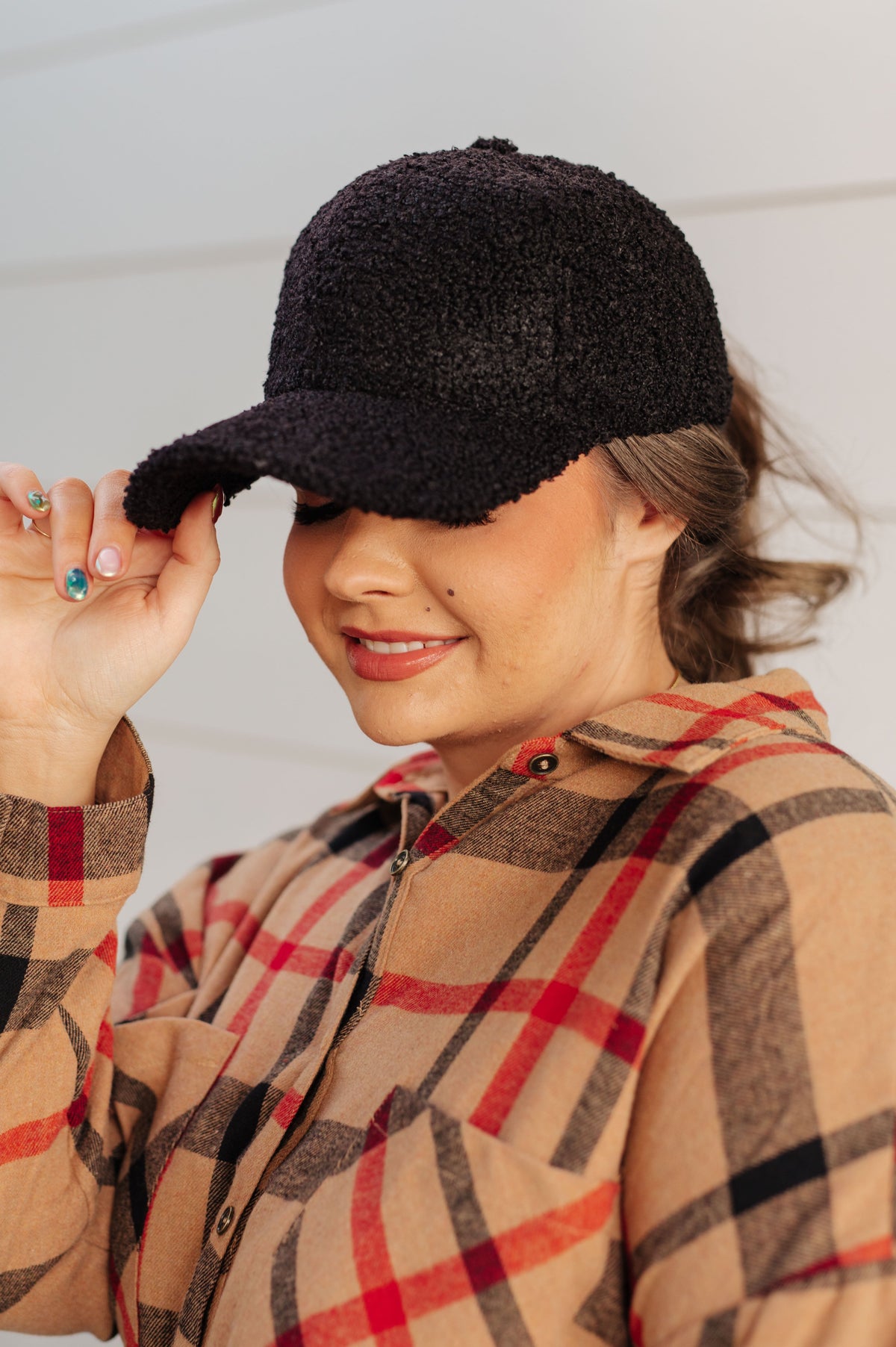 Black sherpa ball cap with a boucle texture and adjustable velcro back on a person wearing a plaid shirt.