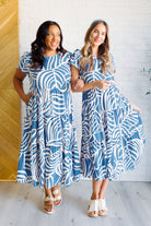 Two woman wearing the Surf Watch Tiered Midi Dress in blue with a white abstract pattern, featuring a round neckline, cap sleeves, and a tiered skirt.