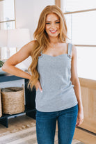 A woman wearing a gray sweetheart neckline tank top with button accents and blue jeans.