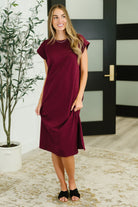 Woman wearing a burgundy dress standing indoors with a plant and door in the background