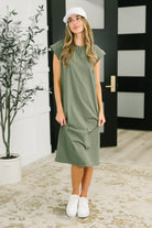 Woman wearing a green dress and white sneakers indoors.