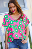 A woman wearing a pink and green flower print V neck short sleeve top with dolman cap sleeves, paired with blue denim shorts.