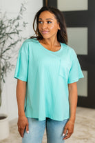A woman wearing a mint green slouchy tee with a round neckline, front pocket, and side slits.