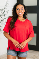 A woman wearing a red slouchy tee with a round neckline, front pocket, and side slits paired with denim shorts.