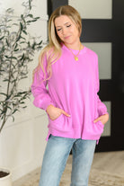 Woman wearing a pink sweatshirt and blue jeans indoors.