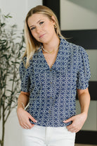 Woman wearing a blue patterned blouse with white pants indoors.