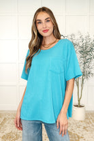 A woman wearing a turquoise colored tee with a round neckline, short sleeves, and a front pocket. The tee has side slits and a banded round neckline.