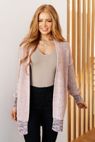 Woman wearing a long, patterned cardigan over a beige top and black pants, standing against a neutral background.