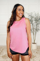 A woman wearing a pink round neck tank top with short sleeves and black shorts.