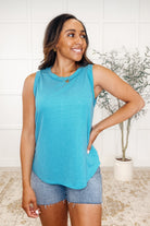 A woman wearing a teal round neck tank top with sleeveless design, paired with high-rise denim shorts.