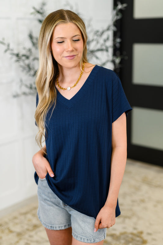 Woman wearing a navy blue top and denim shorts indoors.