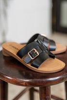 Women's black sandals with a gold buckle on a wooden stool