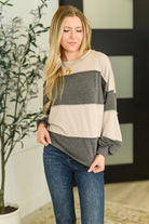 Woman wearing a beige and gray color-blocked shirt with blue jeans indoors.