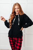 A woman wearing a black bubble knit hoodie with a hood and drawstring, paired with jeans.