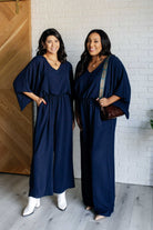 Navy wide leg jumpsuit with V-neckline and kimono sleeves, shown on a model standing indoors.
