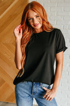 Woman wearing a black top and blue jeans against a white brick wall.