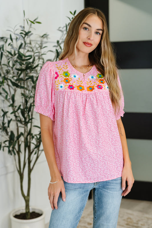 Woman wearing a pink blouse with floral embroidery in an indoor setting