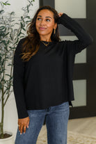 Woman wearing a black shirt top and blue jeans indoors with a plant in the background