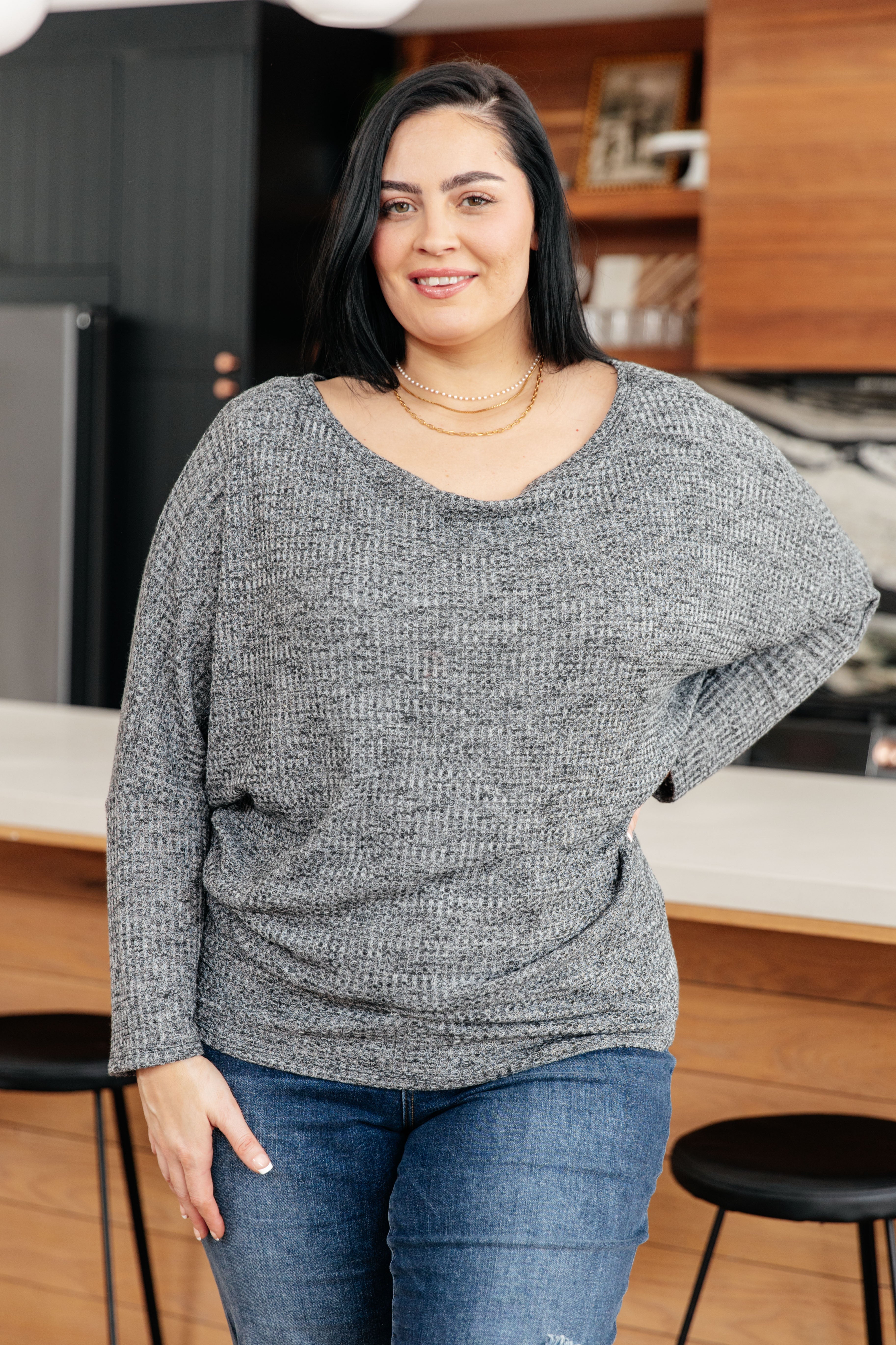 Charcoal ribbed top with boat neckline and dolman sleeves, worn by a model in a kitchen setting.