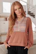 Woman wearing a brown sweatshirt hoodie with a patterned top section in a bright room.