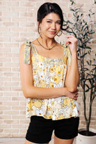 A woman wearing a floral tank top with functional shoulder ties and a front button closure.
