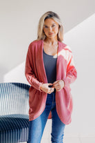 A woman wearing a pink cardigan over a gray top with blue jeans.
