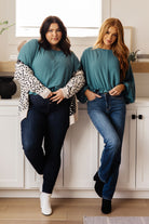 Two models wearing teal tops with batwing sleeves and ruffle details, paired with jeans.