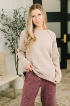A woman wearing a mocha raglan sleeve sweater with ribbed cuffs and hem, featuring side slits and exposed seam details.