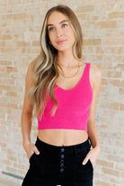 Woman wearing a bright pink tank top against a brick wall.