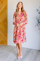 Woman wearing a floral dress standing against a white brick wall.