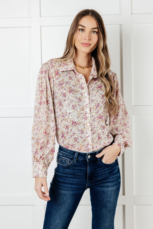 Woman wearing a floral blouse and jeans against a white wall
