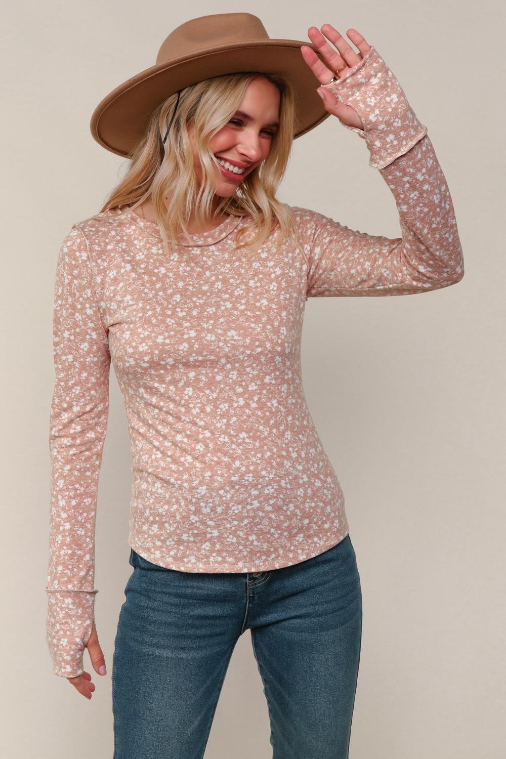 Woman wearing a floral long-sleeve top and wide-brimmed hat against a plain background
