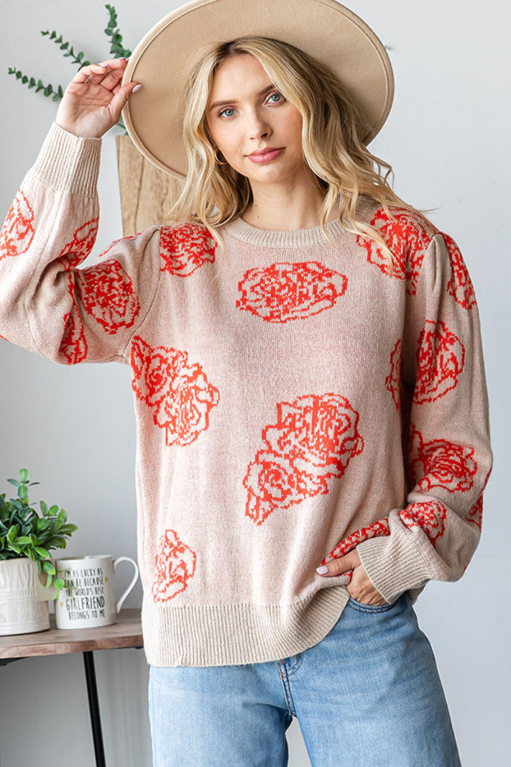 Woman wearing a beige sweater with red floral patterns, standing indoors.