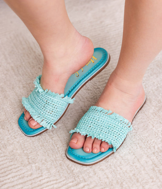 Light blue crochet sandals worn on feet on a textured surface.