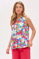 Woman wearing a colorful floral top and pink pants on a white background.