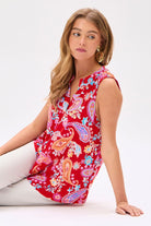 Woman wearing a red floral paisley top sitting on a white background